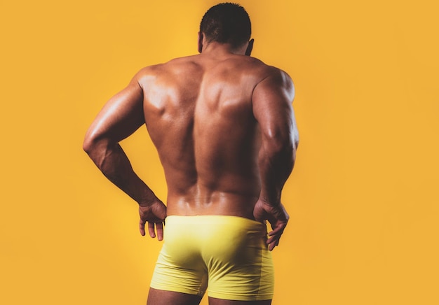 Foto sexy masculino de volta. a vista traseira do torso do construtor de corpo masculino atraente em fundo amarelo. vista traseira de um jovem musculoso nu em cueca calcinha sexy.