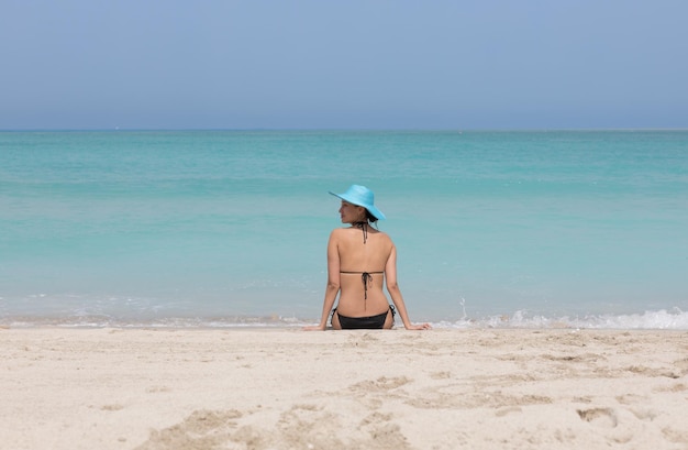 sexy modelo morena en bikini negro y sombrero azul en la playa