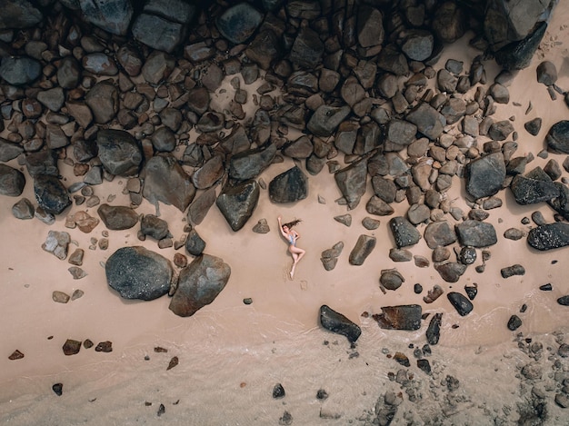 Sexy mujer caucásica en la playa en la arena cerca de las olas y las piedras. Hermosa mujer cubre sus pechos desnudos con sus manos. Phuket. Tailandia Vista aérea superior.