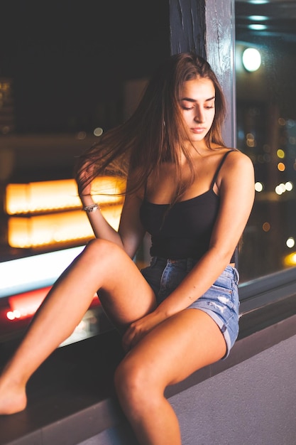 Sexy mujer caucásica con un top negro y pantalones cortos en el borde de un balcón por la noche. Madrid, España.