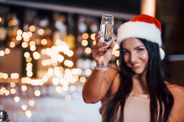 Sexy mujer joven con sombrero de año nuevo y ropa caliente se sienta en el restaurante cerca de la mesa.