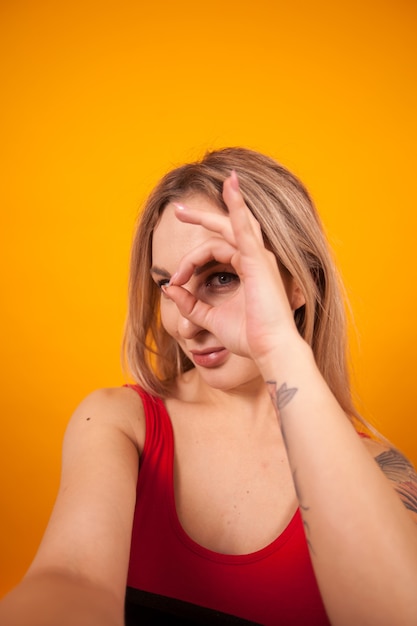 Foto sexy mujer joven en traje de baño rojo haciendo un selfie y mostrando el signo de ok sobre fondo amarillo. hermosa mujer joven en traje de baño.