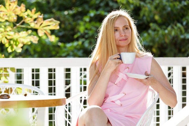 Sexy mujer de mediana edad vestida con un vestido rosa se sienta contra una hoja