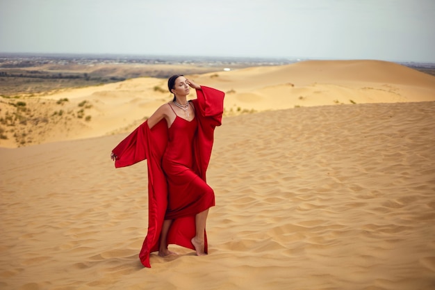 Sexy mujer morena con un vestido largo rojo se encuentra en una duna en el verano en Daguestán