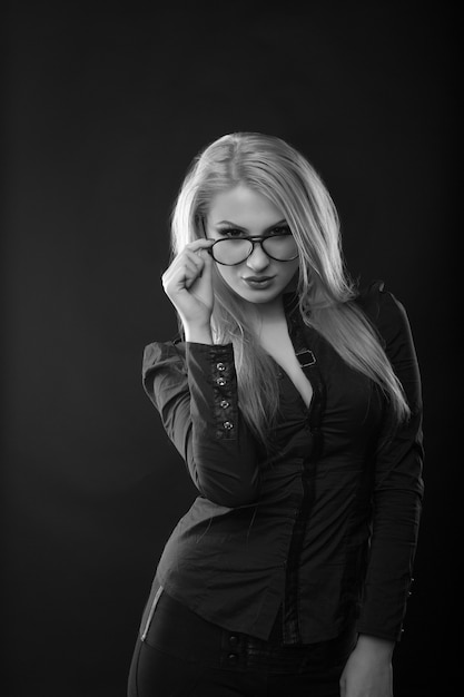 Sexy mujer rubia con pelo largo lleva gafas y blusa posando en el estudio. Disparo monocromo