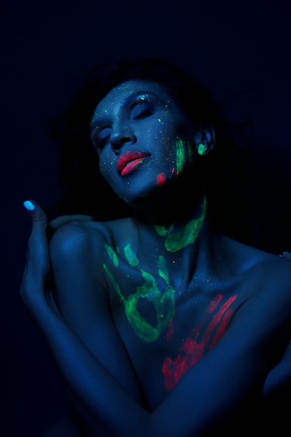 Sexy nackte Frau in Neonlicht, UV-Farbe auf Gesicht und Körper der Frau. Perfekte Figur und Brüste einer Frau, schöne Haare
