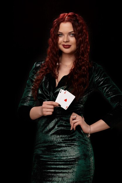 Sexy rothaarige Frau posiert mit Spielkarten in den Händen, auf schwarzem Hintergrund