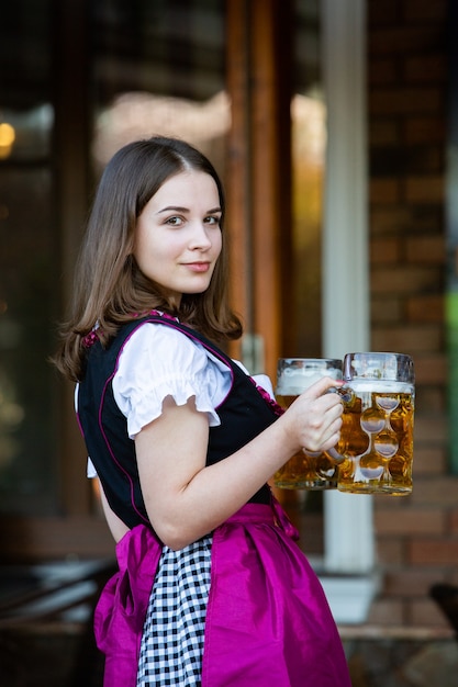 Foto sexy russische frau im bayerischen kleid, das bierkrüge hält