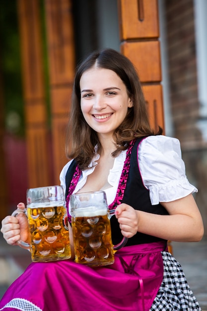 Sexy russische Frau im bayerischen Kleid, das Bierkrüge hält