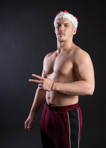 Sexy Santa Claus Fitness Beats demonstriert unwiderstehliche Bauchmuskeln vor schwarzem Hintergrund In a