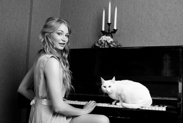 Sexy schönes blondes Mädchen im Kleid, das Klavier mit einer Katze spielt