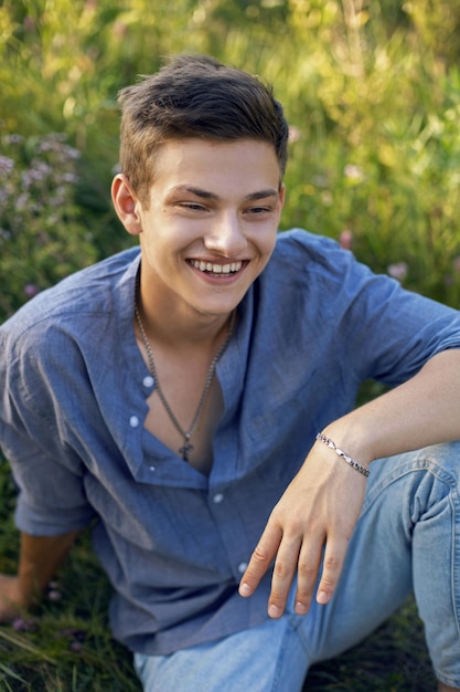 Foto sexy teenager sitzt auf dem gras in der natur in einem hemd und jeans barfuß und schaut barfuß in die kamera