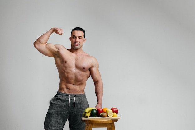 Sexy veganer Kerl mit einem nackten Torso, der neben Obst aufwirft. Diät. Gesunde Ernährung