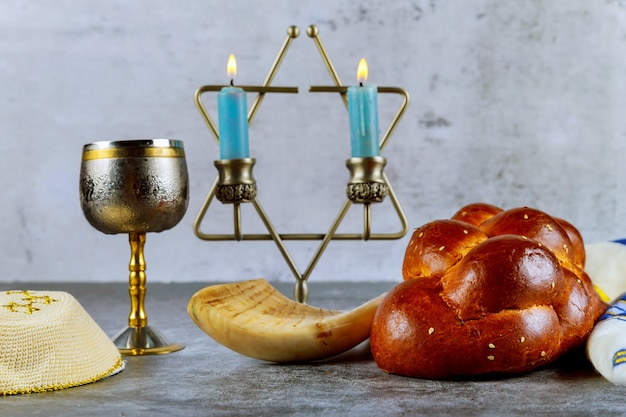 Foto shabat com pão chalá em uma mesa de madeira velas e copo de vinho.