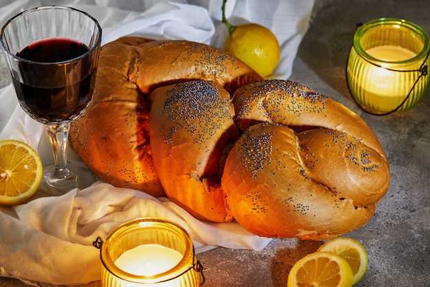 Shabbat Challah mit einer weißen Serviette, mit Kerzen, einem Glas Wein und rustikalen Zitronen. Shabbat Shalom