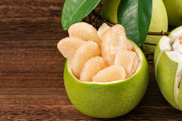 Shaddock de toranja de pomelo descascado fresco com folhas verdes na mesa de prancha de madeira escura Frutas sazonais perto do festival de meados de outono fechar espaço de cópia