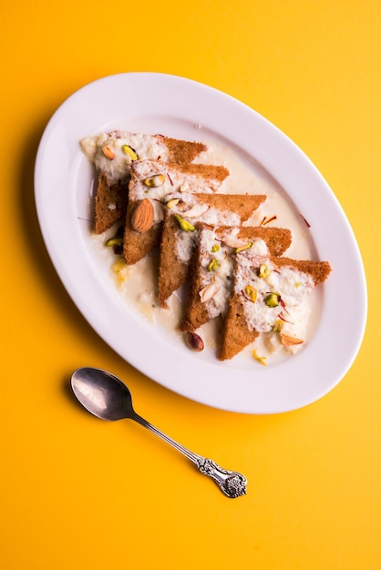 Shahi tukda o Double ka meetha es un budín de pan en ghee, adornado con leche condensada, nueces y mawa / khoya. Postre indio popular, servido en un plato sobre fondo cambiante. Enfoque selectivo