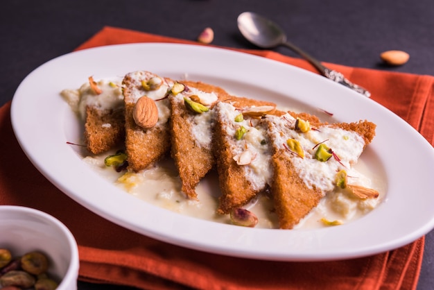 Shahi tukda ou Double ka meetha é um pudim de pão com ghee, guarnecido com leite condensado, nozes e mawa / khoya. Sobremesa indiana popular, servida em um prato sobre um fundo temperamental. Foco seletivo