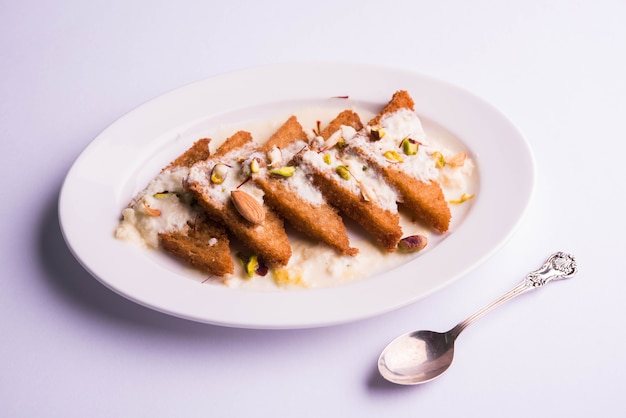 Shahi tukda ou Double ka meetha é um pudim de pão com ghee, guarnecido com leite condensado, nozes e mawa / khoya. Sobremesa indiana popular, servida em um prato sobre um fundo temperamental. Foco seletivo