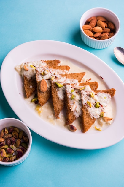 Shahi tukda ou Double ka meetha é um pudim de pão com ghee, guarnecido com leite condensado, nozes e mawa / khoya. Sobremesa indiana popular, servida em um prato sobre um fundo temperamental. Foco seletivo