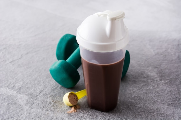 Shake de proteína de chocolate e halteres em pedra cinza