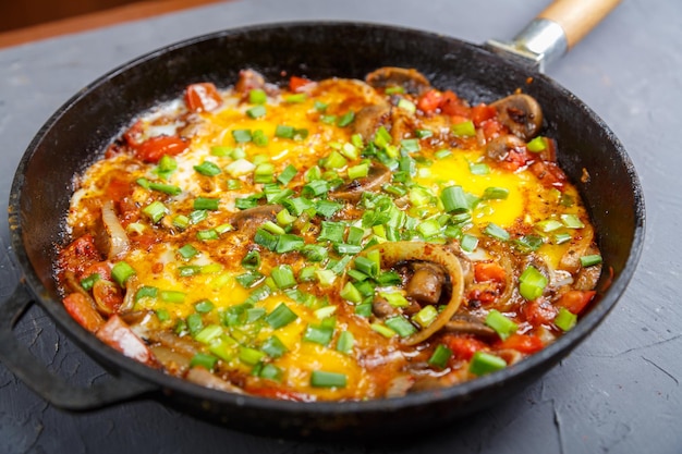 Shakshuka caliente con hierbas en una sartén sobre una mesa gris