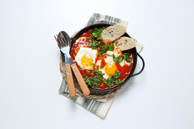 Shakshuka com dois pedaços de pão colher e garfo na toalha vista superior de fundo branco