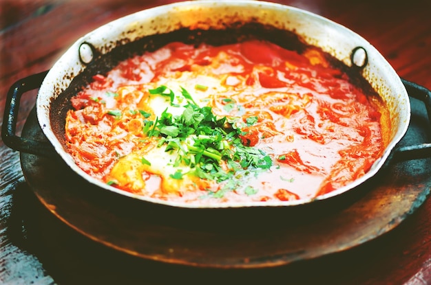 Shakshuka Comida judía tradicional y receta de cocina de Oriente Medio Huevos fritos tomates pimiento y perejil en una sartén Primer plano enfoque selectivo Efecto tonificado