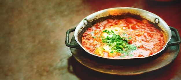 Shakshuka Comida judía tradicional y receta de cocina de Oriente Medio Huevos fritos tomates pimiento y perejil en una sartén Primer plano enfoque selectivo Efecto tonificado