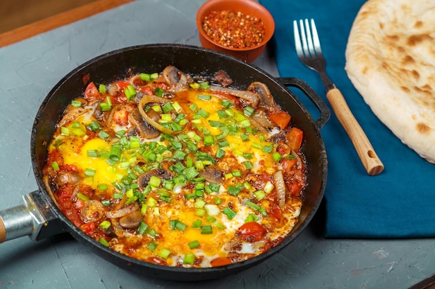 Shakshuka em uma frigideira em um fundo cinza ao lado de um garfo em um guardanapo azul