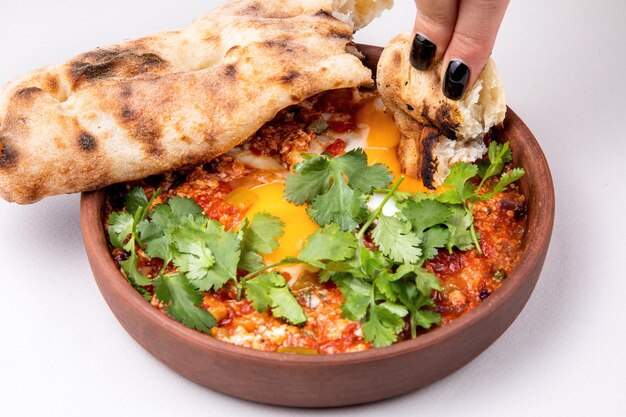 Shakshuka con hierbas, queso y bollería fresca sobre un fondo claro