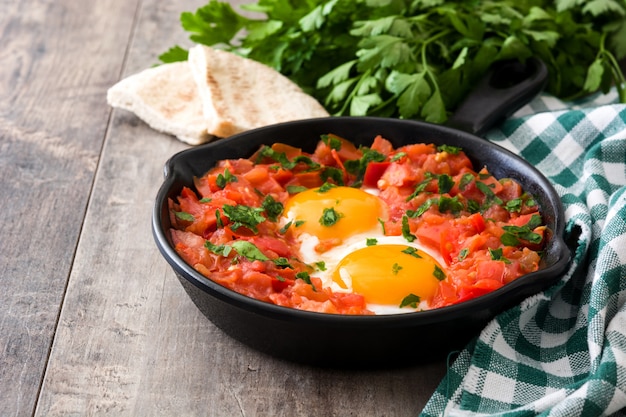 Shakshuka en sartén de hierro sobre mesa de madera Comida típica en Israel.