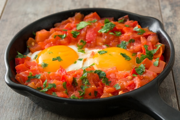 Shakshuka en sartén de hierro sobre mesa de madera Comida típica en Israel.