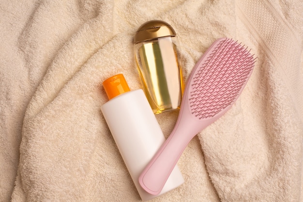 Shampoo, pente e óleo de cabelo revitalizante deitado sobre uma toalha amassada em um banheiro. Copie o espaço