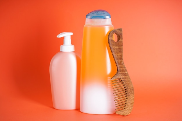 Shampooflasche, Seifenspender, eine hölzerne Haarbürste auf orangefarbenem Hintergrund.