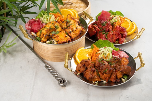 Shashlik de frango, bovino e porco com guarnição de vegetais e temperos picantes, cozido em tandoor. um conjunto de três pratos de carne quente em pratos tradicionais indianos.