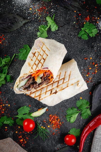 Shawarma Burrito geschnitten mit Gemüse und Kräutern auf einem dunklen Steintisch Das Konzept von Fast-Food-Restaurants