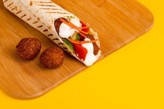 Shawarma com falafel em uma vista lateral de tábua de madeira em um fundo amarelo