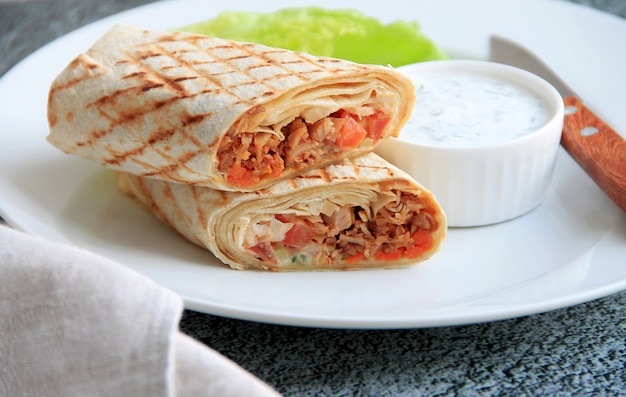 shawarma com frango, legumes e ervas em um prato branco ao lado do molho e faca