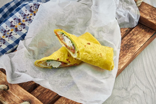 Shawarma dietético rollo de salmón ligeramente salado y queso crema en pan de pita amarillo sobre pergamino y una bandeja de madera. De cerca, comida rápida