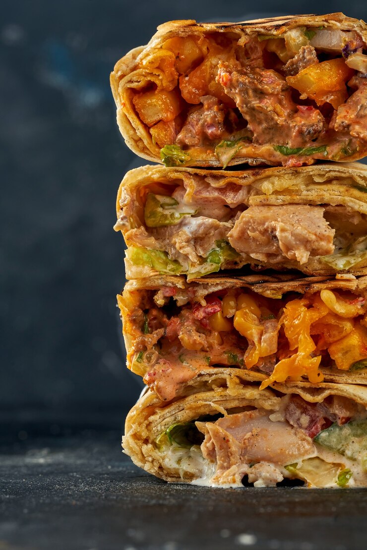 Foto shawarma empilhou um em cima do outro com recheio de carne e vegetais. uma pilha de shawarma em um fundo escuro. foco seletivo