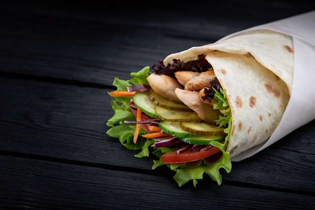 Shawarma enrollado en lavash, carne húmeda a la parrilla con cebolla, hierbas y verduras sobre superficie de madera negra