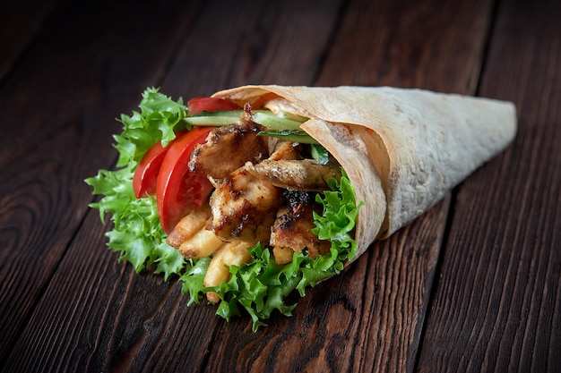 Shawarma enrollado en lavash con carne a la parrilla y verduras sobre fondo de madera