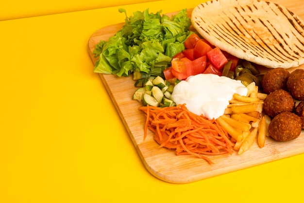 Shawarma con falafel en una vista lateral de tablero de madera sobre un fondo amarillo