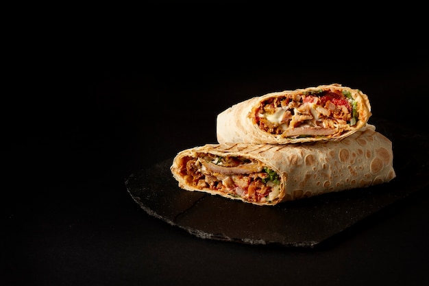 Shawarma, in Lavash rollen, gegrilltes Fleisch, mit Gemüse, Sandwich, auf einem schwarzen Tisch geschnitten, horizontal, Spase kopieren