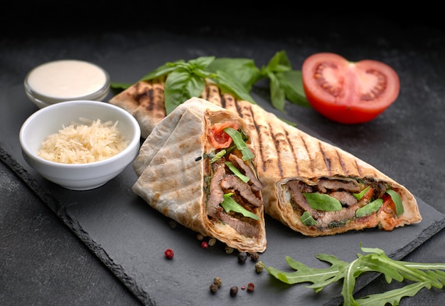 Shawarma mit Fleisch, Cutaway, mit Sauce, Tomaten, Käse, Kräutern und Knoblauch, auf schwarzem Schiefer, auf schwarzem Hintergrund