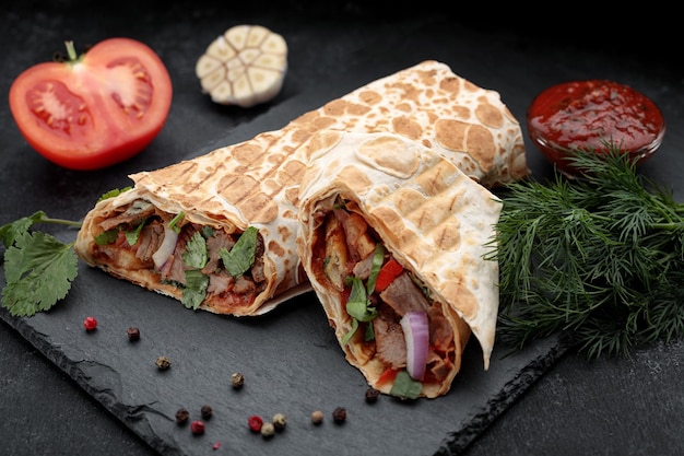 Shawarma mit Kalbfleisch mit Sauce und Dill im Hintergrund auf schwarzem Hintergrund