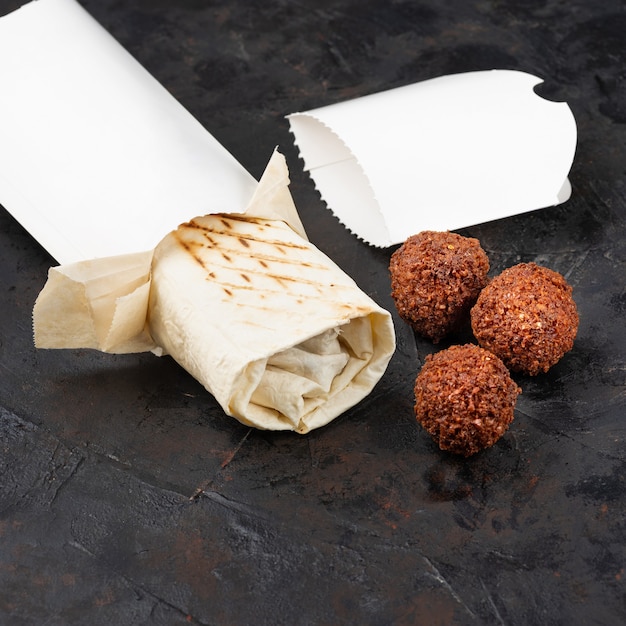 Foto shawarma oriental tradicional con chuletas de falafel frito sobre un fondo negro. refrigerios saludables o almuerzo para llevar. concepto de eco-envases para materiales reciclables. copia espacio