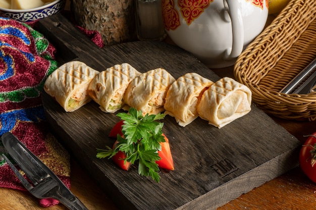 Shawarma con pollo, verduras y tomate fresco cortado en trozos sobre una tabla de cortar de madera