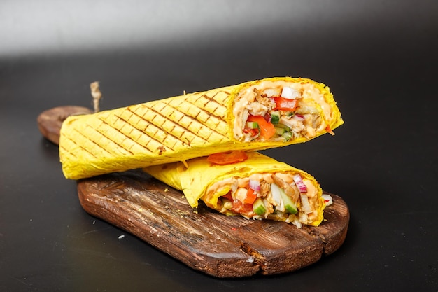 shawarma de queso en pan de pita amarillo con carne frita y verduras en una tabla vieja de corte de madera